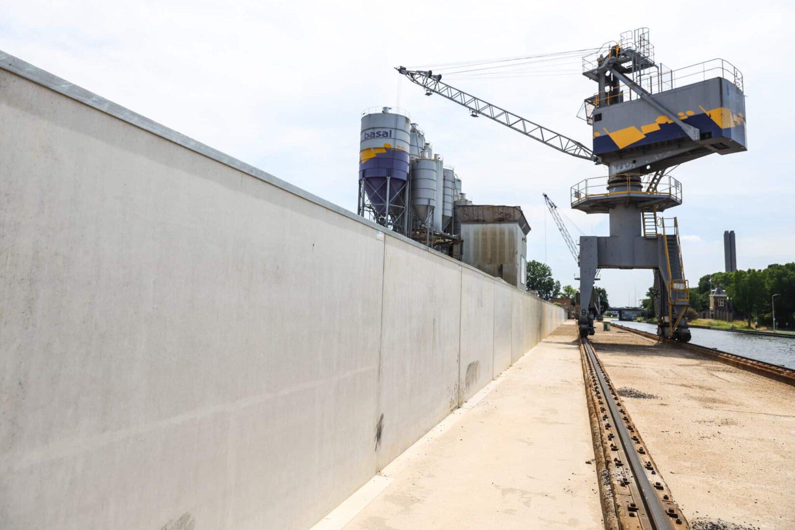 Betonstützwand als Geländeumzäunung entlang einer Hafenanlage mit Verladekran